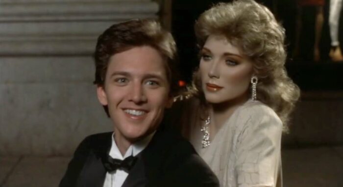 A smiling white man with a blond mannequin in a fancy white dress and jewelry behind him