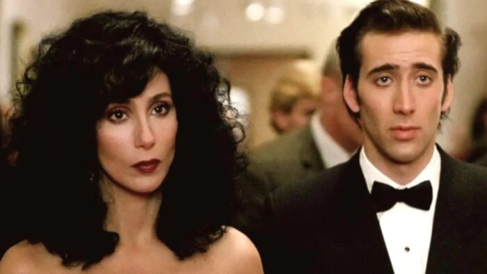 A woman with long curly black hair (Cher) standing next to a man in a tuxedo (Nicholas Cage)