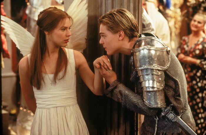 A teenage boy wearing a knight in armor costume is kissing the hand of a teenage girl in an angel costume with wings.