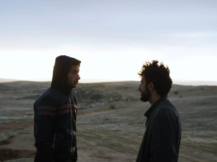 A photo of two men facing each other, in a desert-like landscape with low light