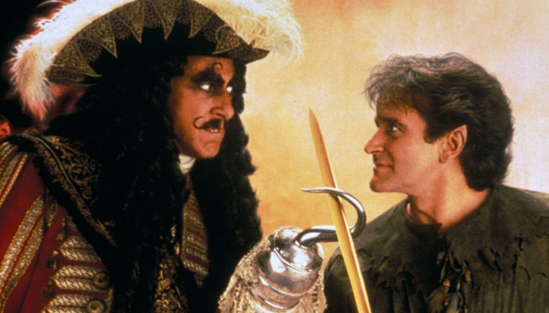 A man in a pirate outfit with a hook for a hand looking threateningly at a man with short brown hair holding a sword.