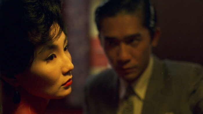 A beautiful woman's face looking sadly to the side. A man in a suit is looking intently at her face a few feet away.