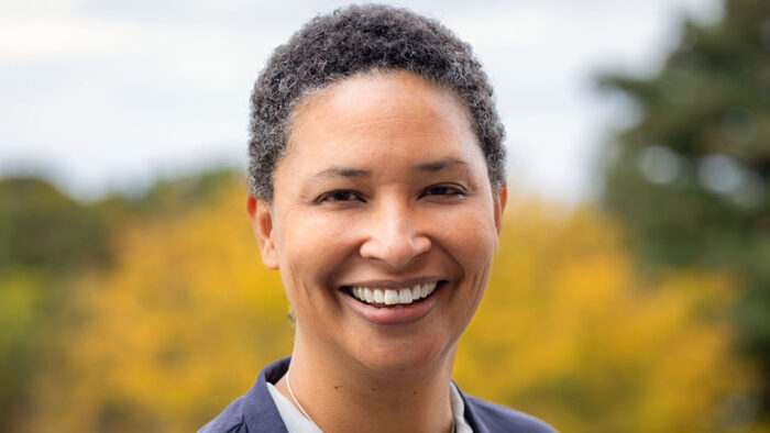 Close up portrait of a smiling Black woman with short hair with trees behind her