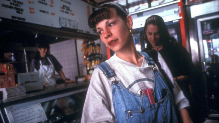 Film still of a young woman wearing a baggy t-shirt and overalls in front of a restaurant counter