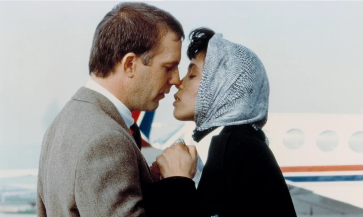 A white man with short brown hair (Kevin Costner) about to kiss a Black woman with a light blue headscarf on (Whitney Houston)