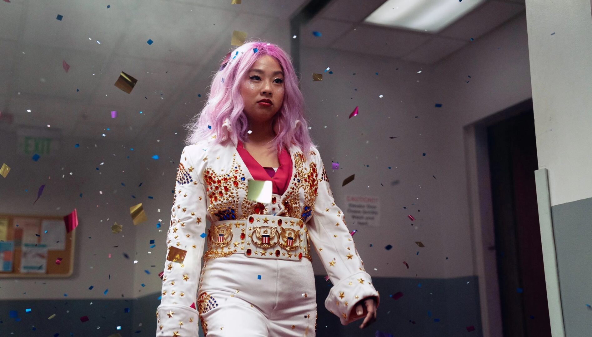 A young woman wearing a long pink wig and a white Elvis jumpsuit with confetti in the air around her