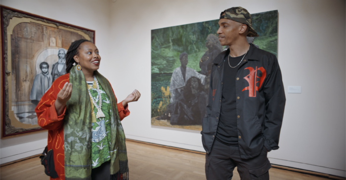 A photo of two young Black people standing in a gallery--the curator Intisar Abioto and the filmmaker Devin Boss