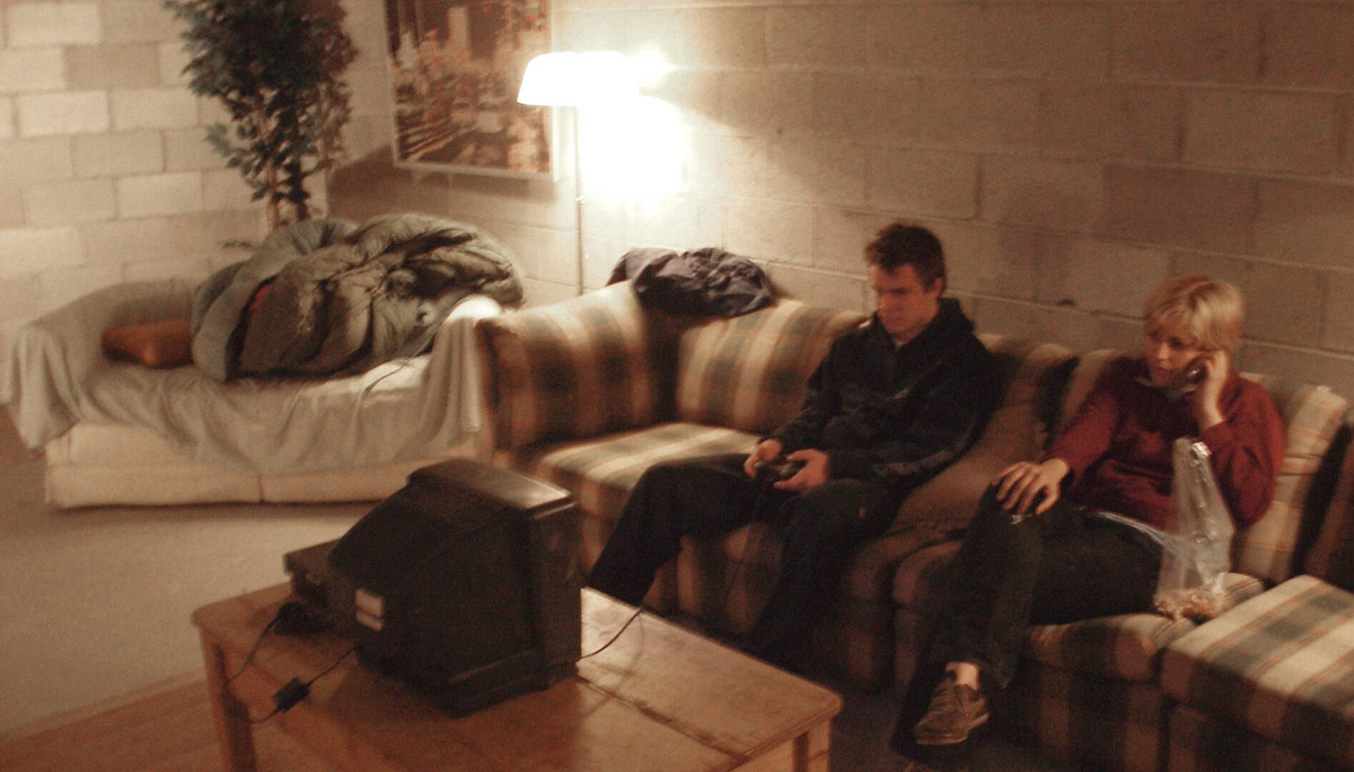 Two people sitting on a couch, looking at a small television, in a concrete block room.