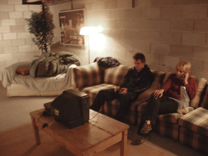 Two people sitting on a couch, looking at a small television, in a concrete block room.