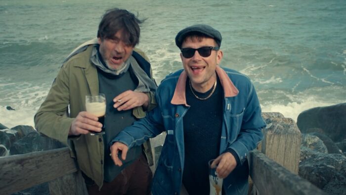 Two men holding pints of beer and smiling in front of the ocean