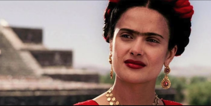 Salma Hayek dressed as artist Frida Kahlo standing in front of a pyramid.