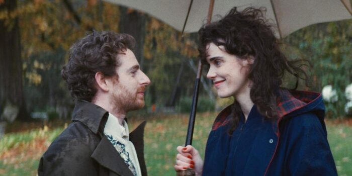 A man and a woman, both with curly brown hair, looking at each other under an umbrella
