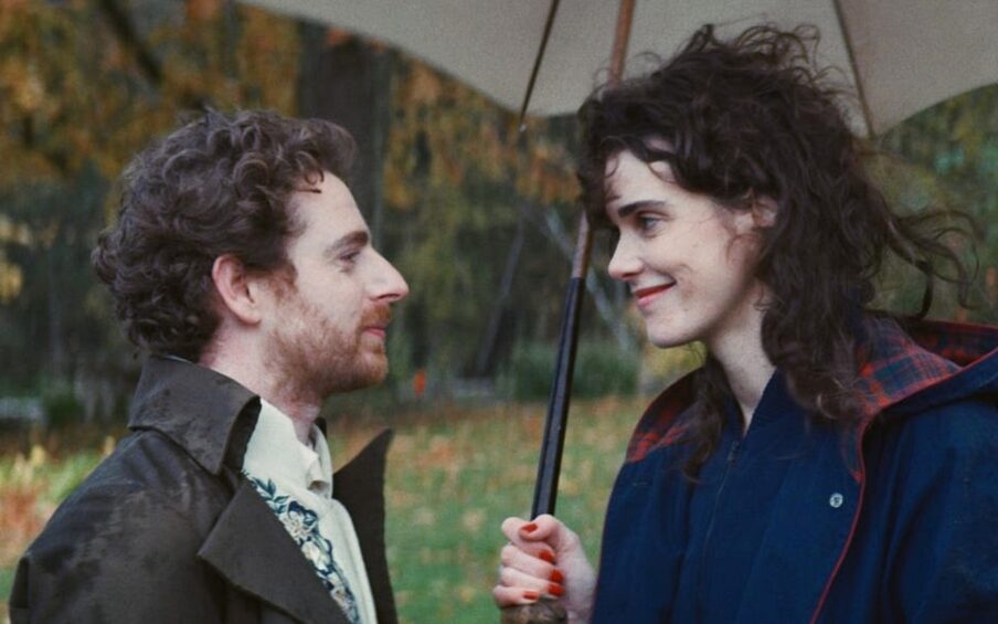 A man and a woman, both with curly brown hair, looking at each other under an umbrella