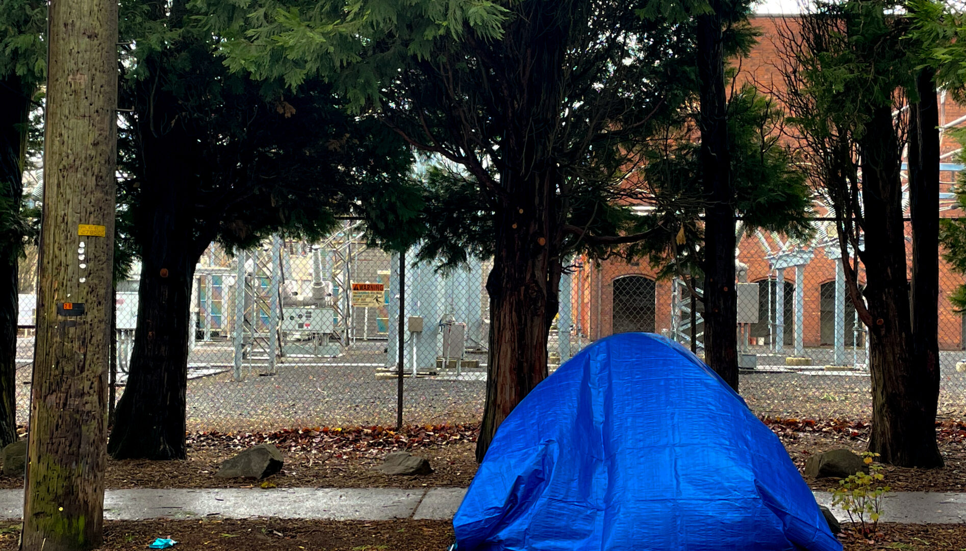 Photo of a sidewalk with a tent and a blue tarp over it.