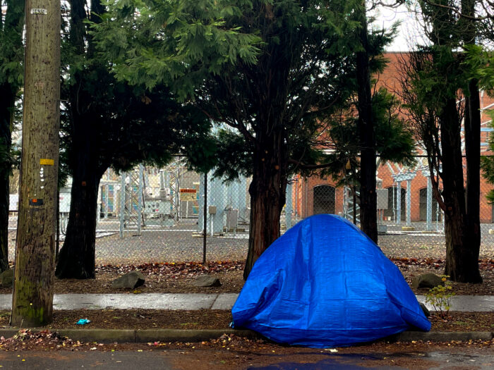 Photo of a sidewalk with a tent and a blue tarp over it.