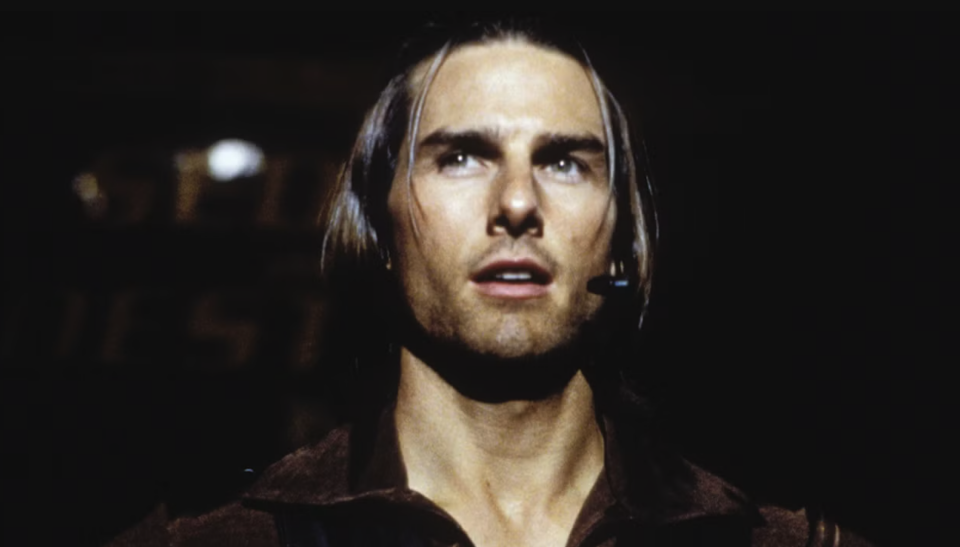 A film still of a white man with long brown hair (Tom Cruise) wearing a wireless microphone.