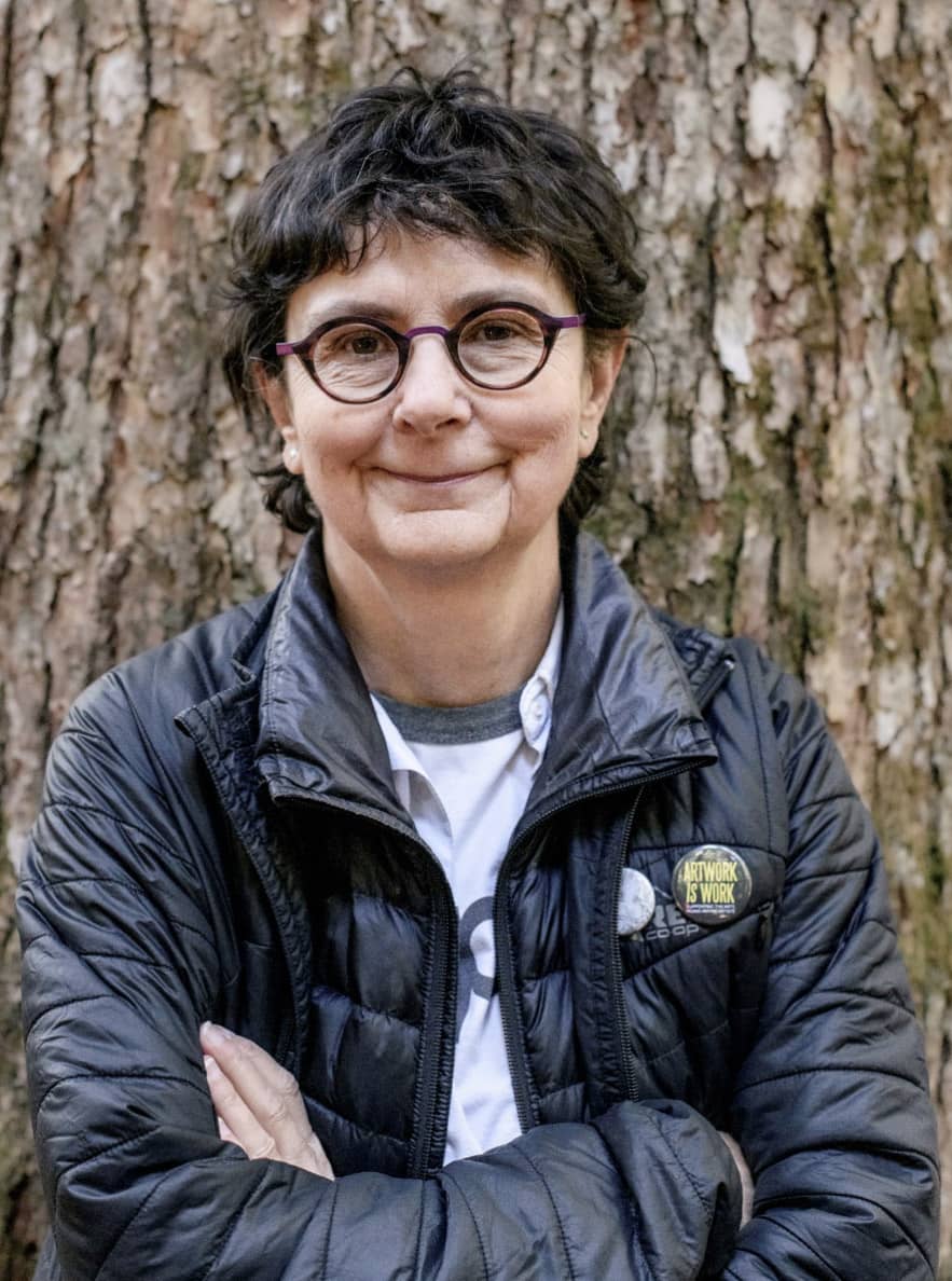 A person standing with arms crossed in front of a tree.