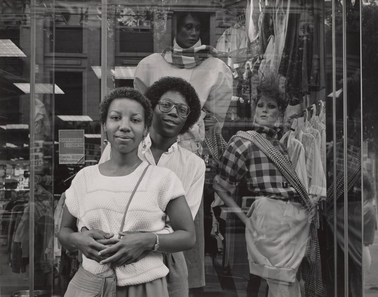 Two people standing in front of a shop window with a mannequin in the display.