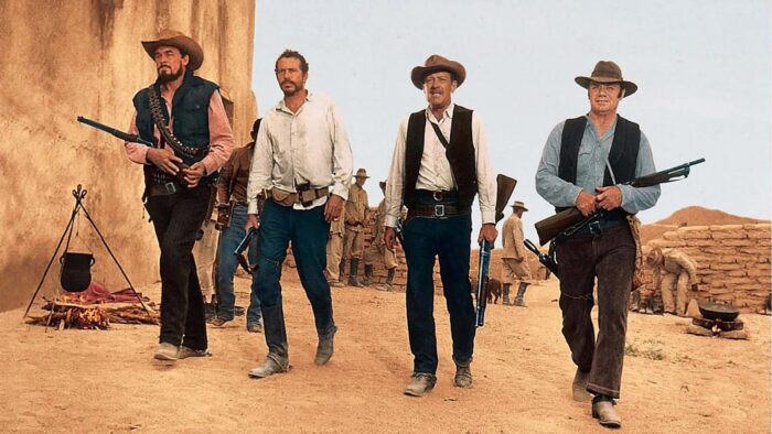 Four men in old "Western" outfits holding rifles.