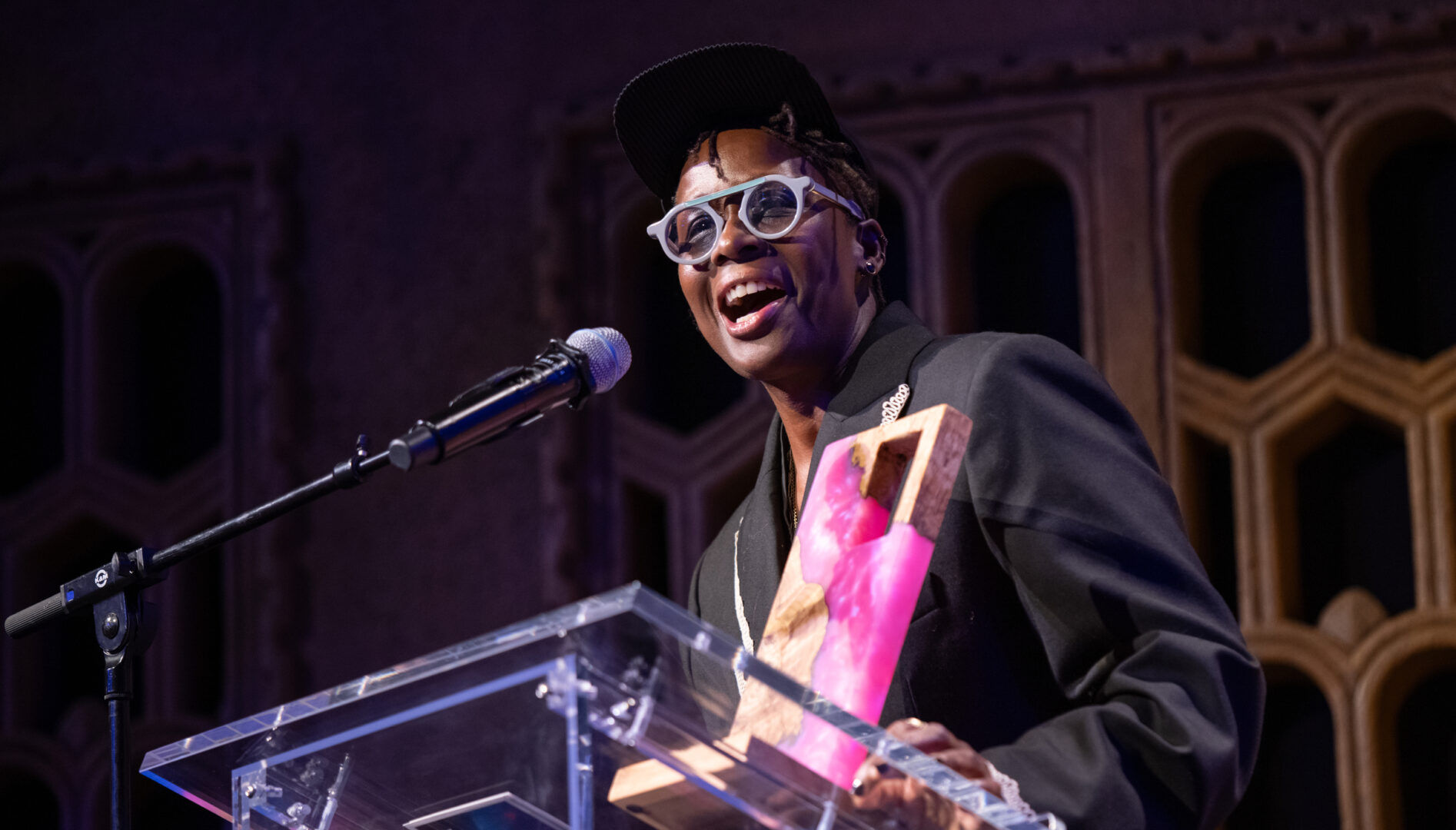 Photo of the artist Mickalene Thomas standing at a podium, holding a Cinema Unbound award, and speaking into a microphone.
