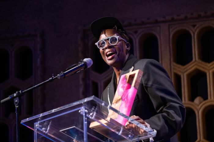 Photo of the artist Mickalene Thomas standing at a podium, holding a Cinema Unbound award, and speaking into a microphone.