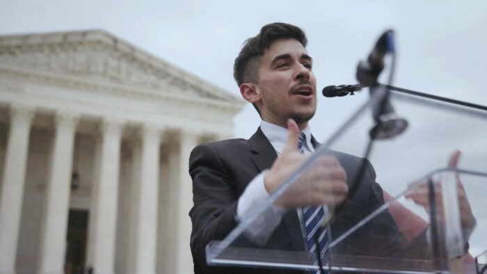 A man stands speaking at a podium in front of the U.S. Supreme Court building.