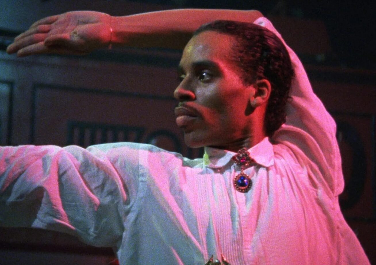 A Black man in a white button-down shirt voguing.