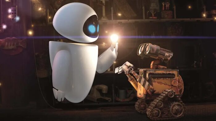 Animated film still of a futuristic looking white robot holding up a glowing light bulb in front of an older, work looking robot.