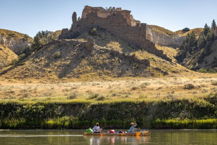 Film still of a Black man and a Black woman on a canoe on a river in front of a high desert butte and land.