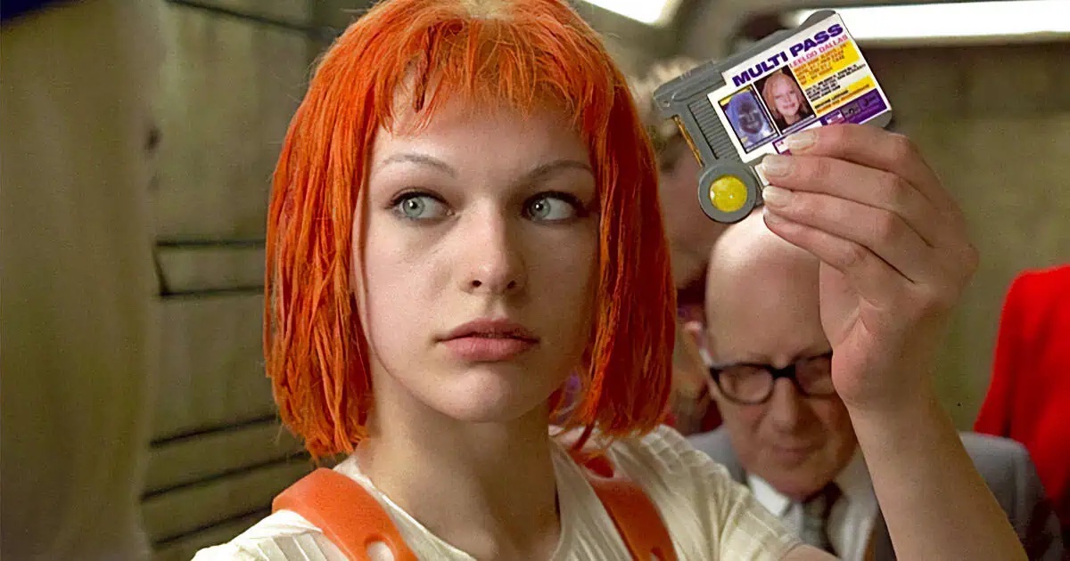 Film still of a white woman with an orange-red dyed bob haircut, holding up an ID card.