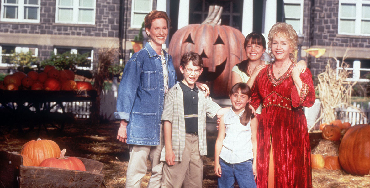 An multigenerational group of white people standing outside in an autumnal setting, with a big pumpkin behind them.