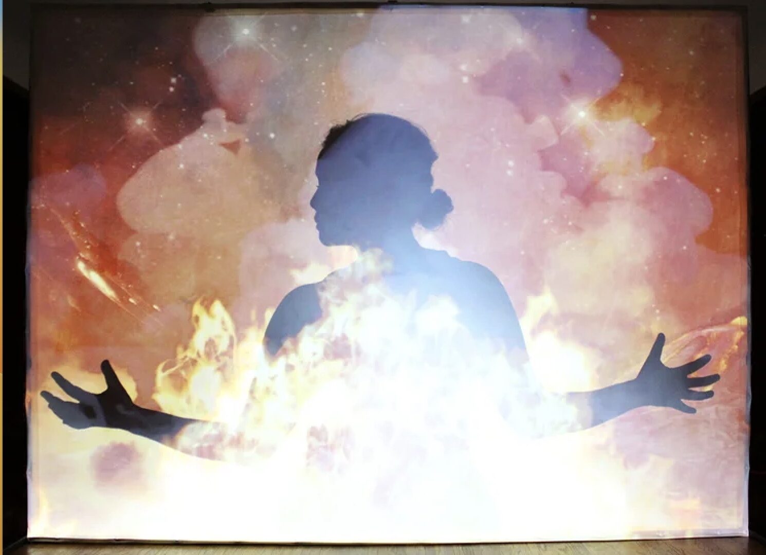 Outline of a woman with her arms out and face turned to the left. In front of her are flames and smoke.