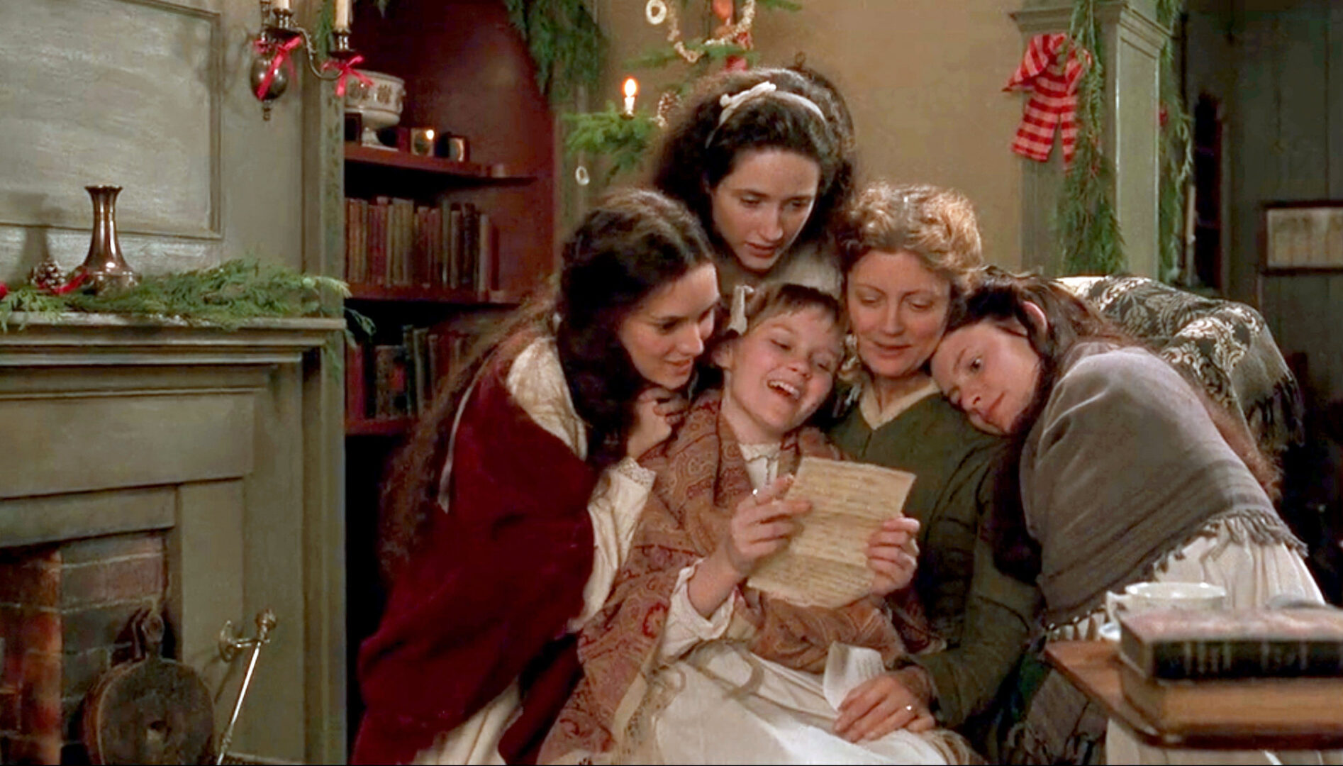 A group of women and girls in a room with Christmas decorations. They are gathered together looking at a letter that one girl is holding.