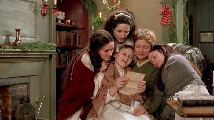 A group of women and girls in a room with Christmas decorations. They are gathered together looking at a letter that one girl is holding.