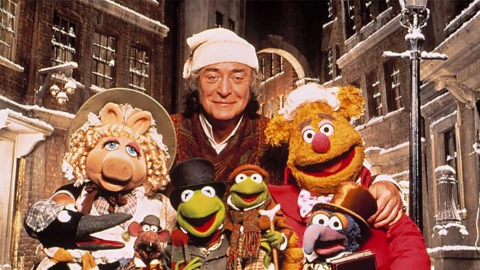 Film still of a group of Muppets with an older white man in a white stocking cap.