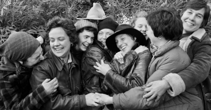 A black and white photo of a group of women smiling, laughing, and hugging.