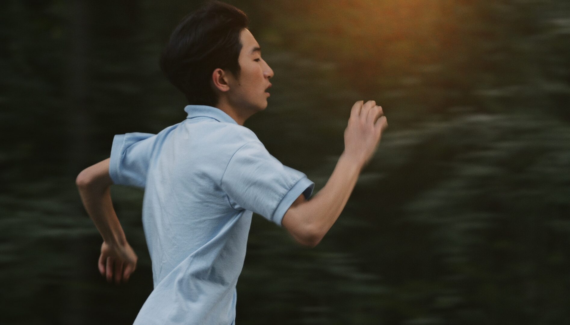 Film still of a young man in a light blue, short-sleeved shirt running.