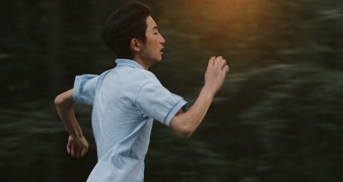 Film still of a young man in a light blue, short-sleeved shirt running.