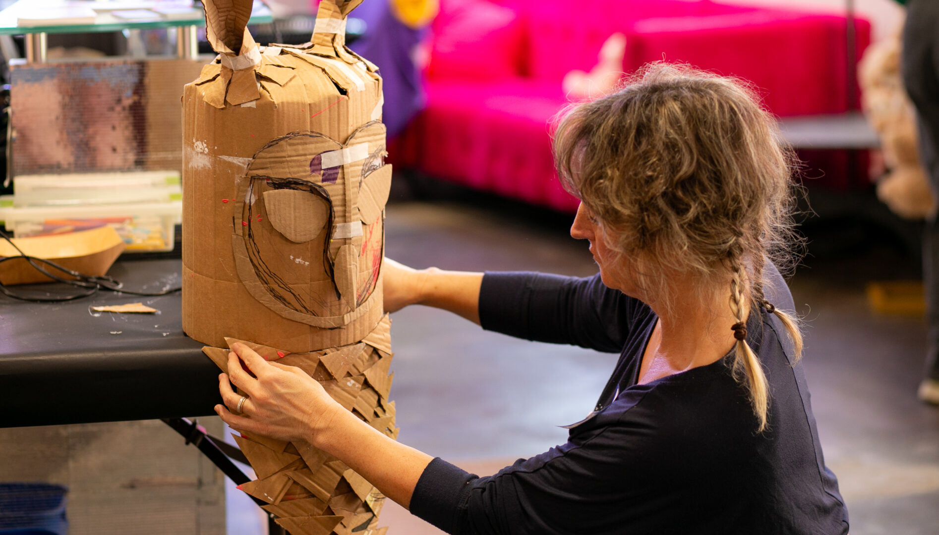 Photo of a woman with blonde hair and a dark blue shirt working on a cardboard owl mask
