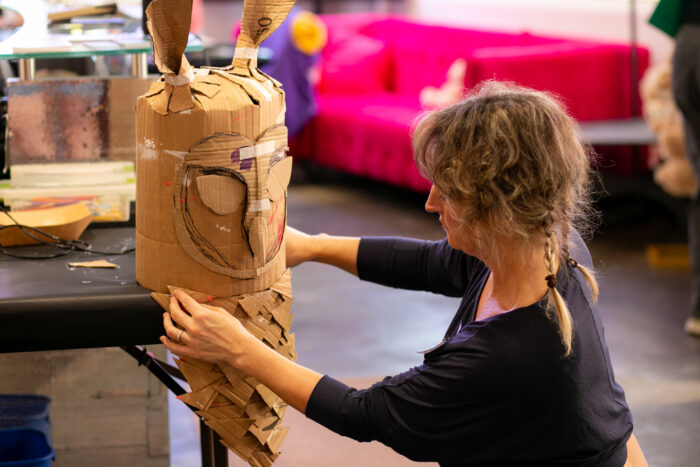 Photo of a woman with blonde hair and a dark blue shirt working on a cardboard owl mask