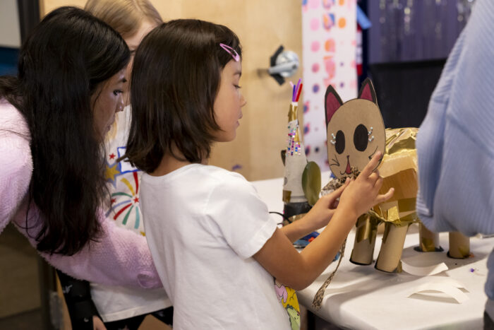 A young girl with dark brown hair works on a cardboard cat that she's crafting.