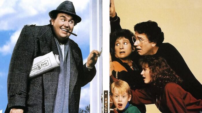 Film still of a man in a trenchcoat, hat, and suit, with a newspaper under his arm and cigar in his mouth, knocking at a white door. On the other side of the door are two adults, a teenager, and a kid looking scared.