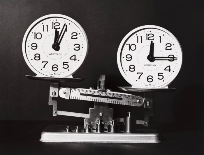 Two analog clocks sitting atop a balancing scale.