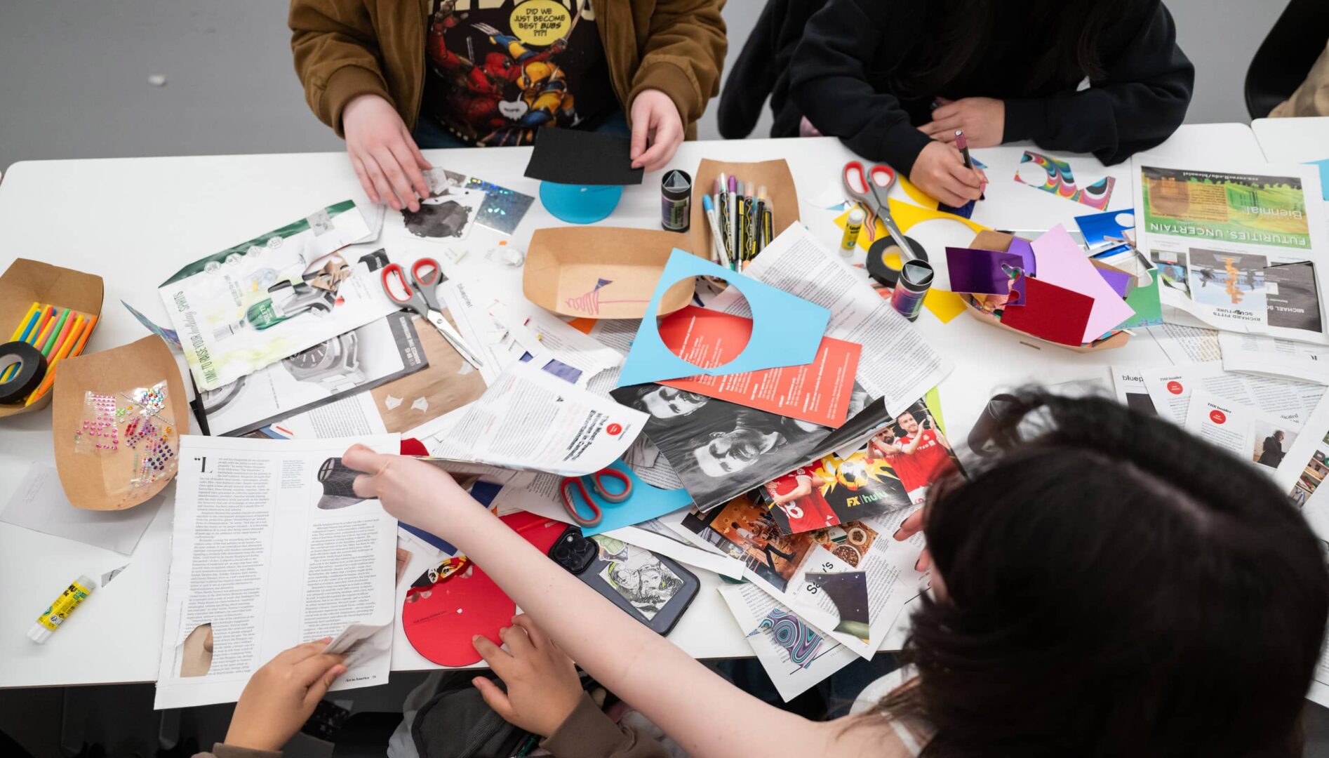 People sitting around a table with a mix of papers and crafting tools.