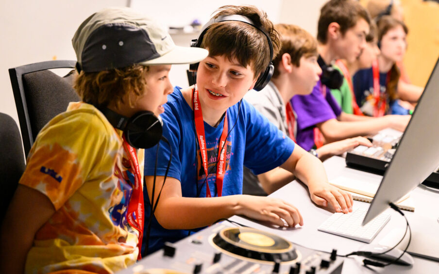 Two kids working together at a computer and DJ mixing equipment.