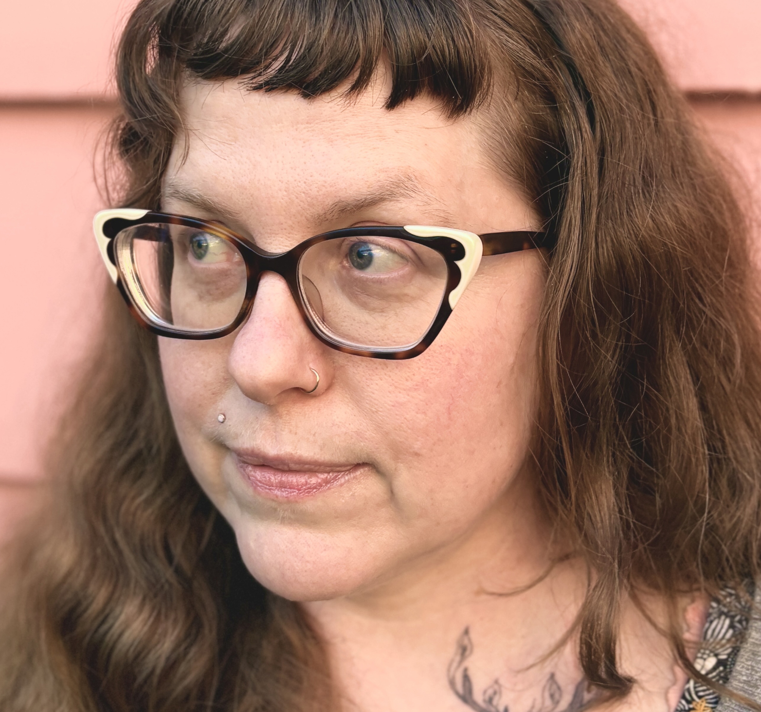 Close-up photo of a woman with long brown hair and short bangs. She is wearing vintage-looking eyeglasses.
