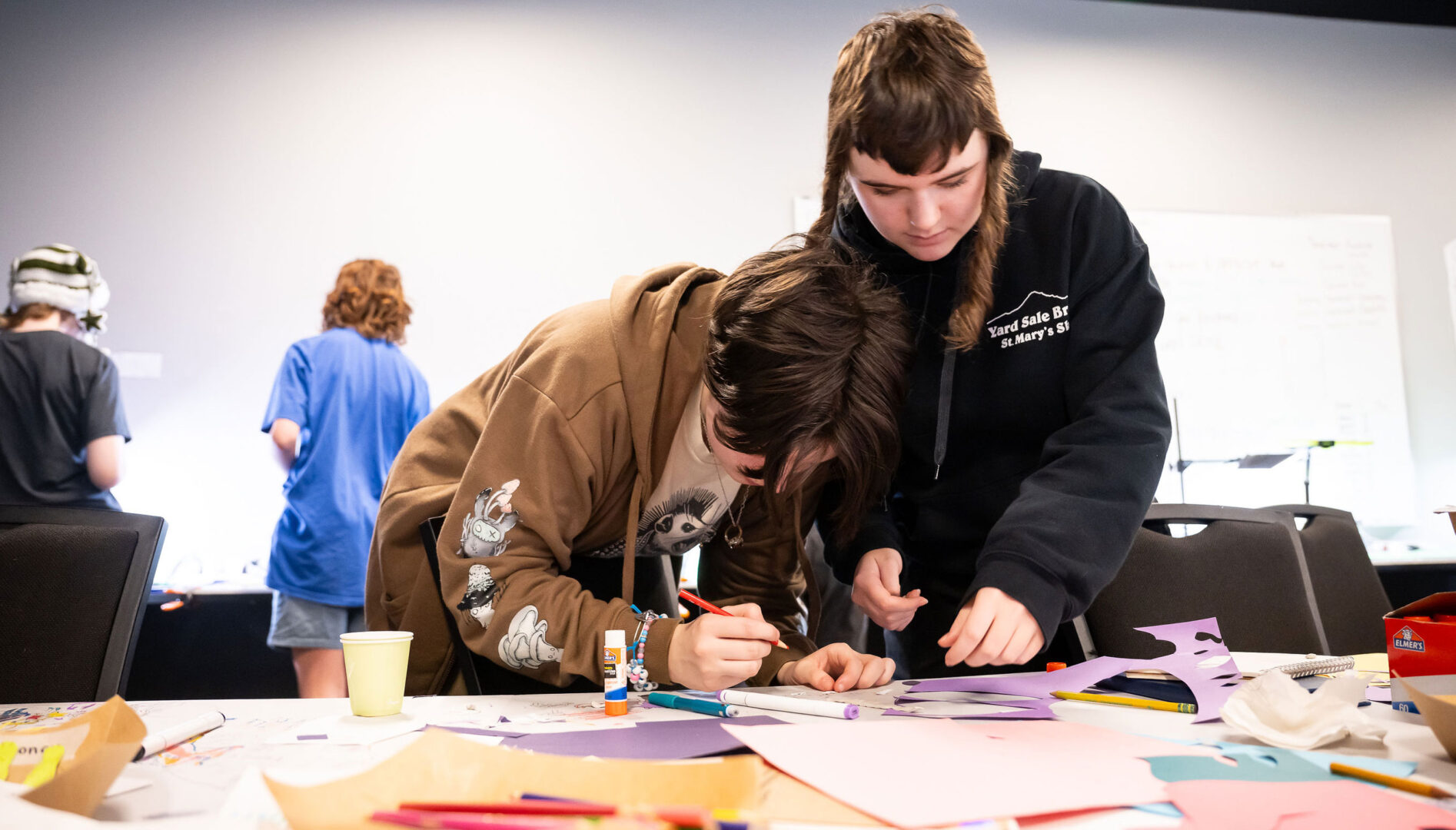 Two kids working together at a table full of art supplies.