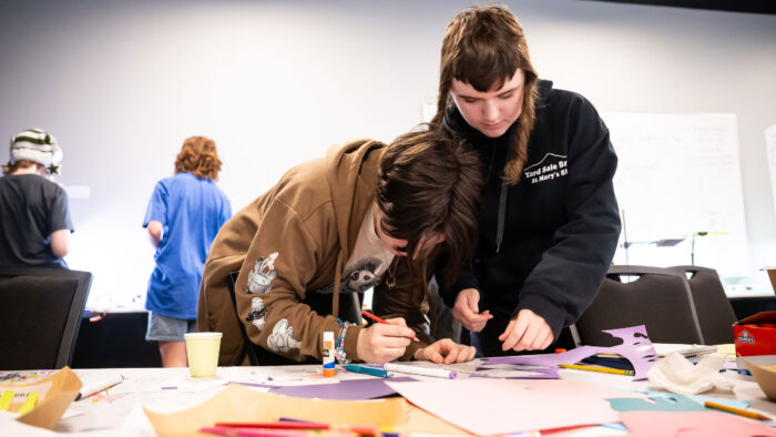Two kids working together at a table full of art supplies.