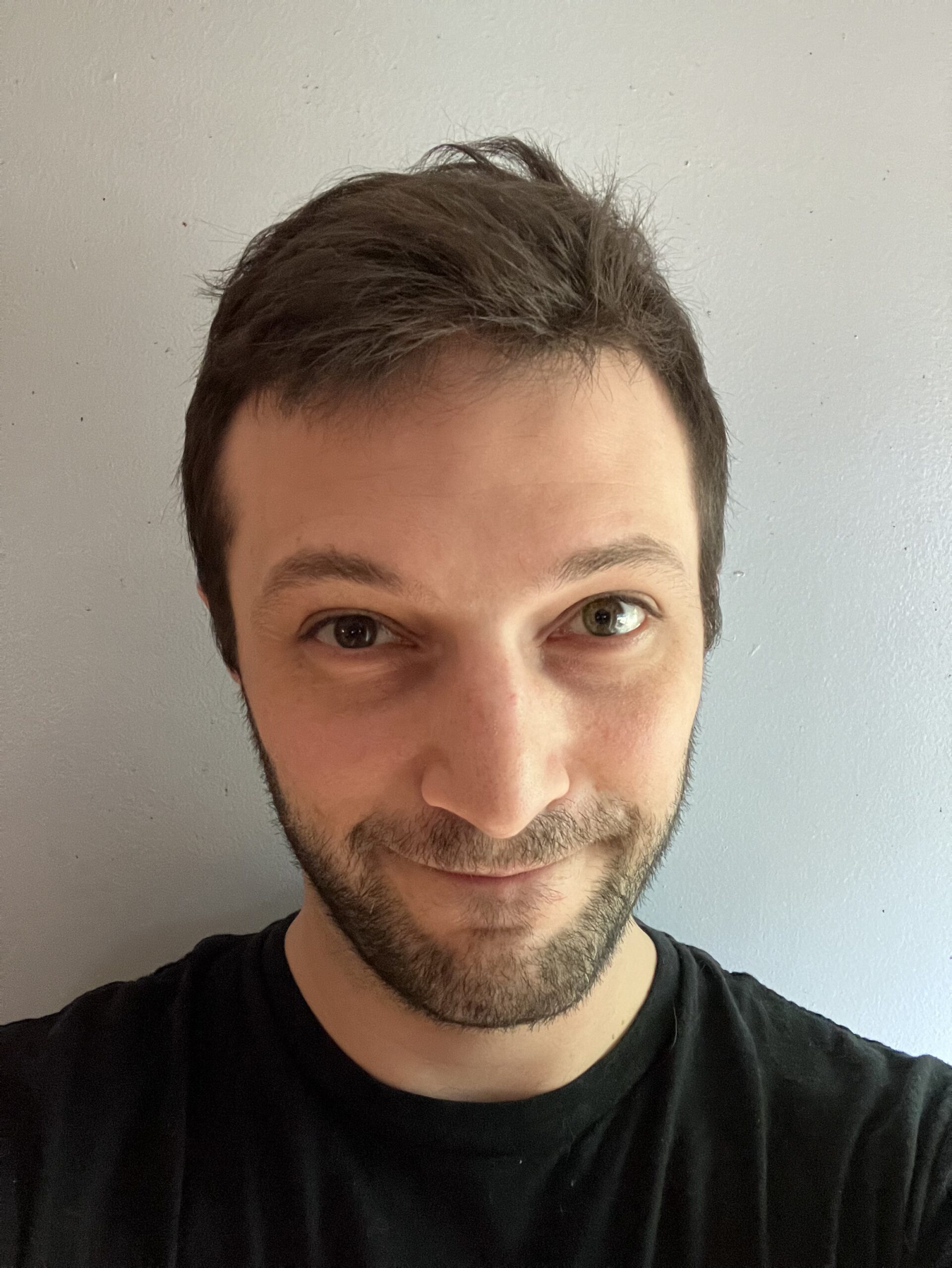 Close-up portrait of a smiling man with dark brown hair and a five-o-clock shadow of facial hair.