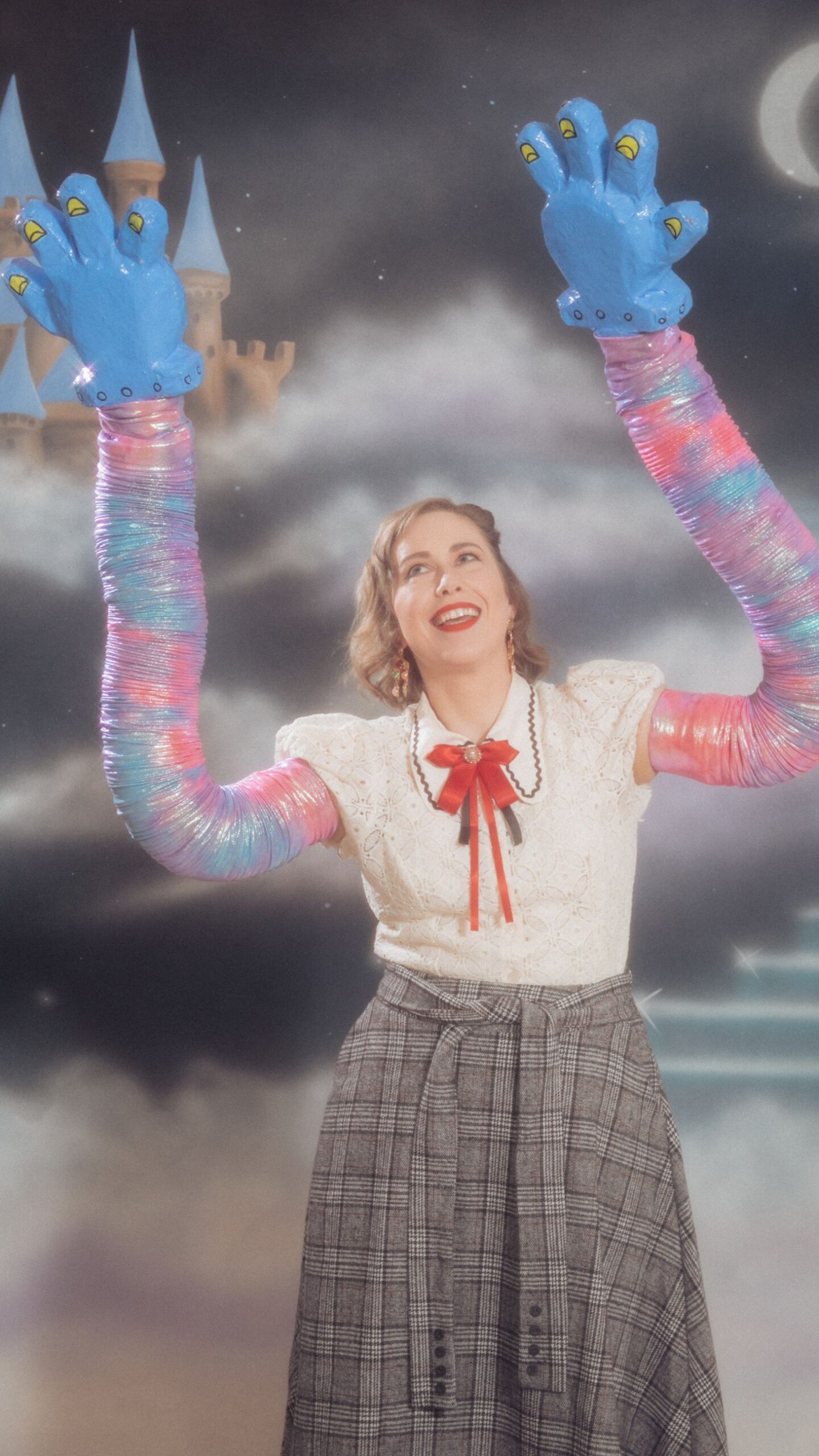 Photo of a person with clouds behind them and large colorful fake arms and hands in the air